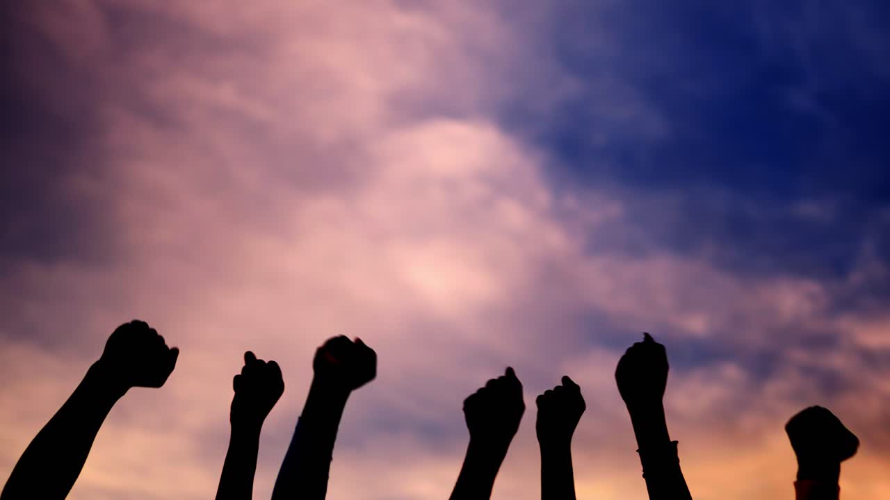 Silhouette of Fists Raised in Protest Against a Dramatic Sky