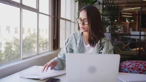 mujer creativa asiática del milenio sentada en un escritorio trabajando en una computadora portátil en una oficina casual, de cerca