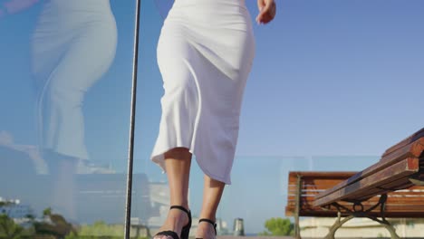 female model in white long dress walk near glass safety barrier, mallorca