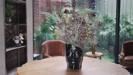 jarrón negro artístico con flores secas en una mesa de madera en un entorno interior moderno