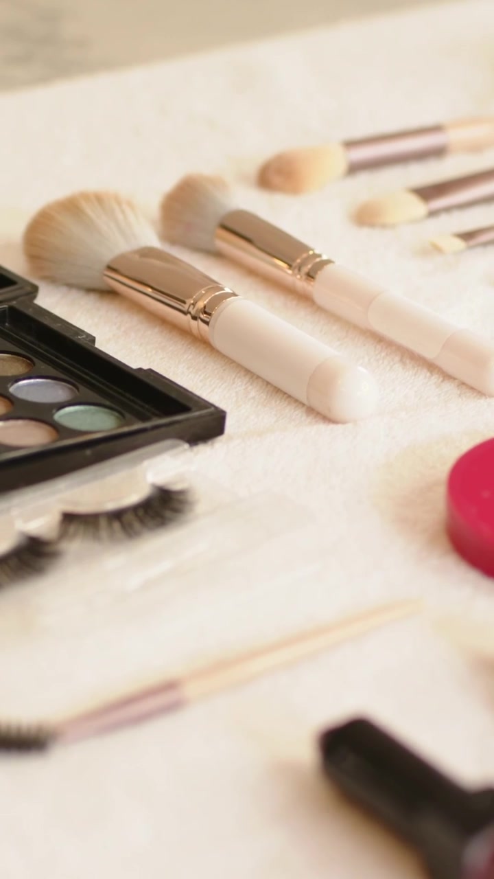 Vertical video: Sliding camera revealing 3 lipsticks, compact palette, brushes and lashes on vanity