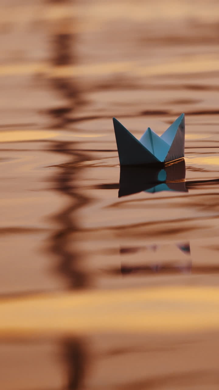 Two blue paper ships on water outdoors. Origami boats floating on the water surface in the evening. Close-up. Vertical video