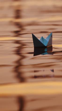 two blue paper ships on water outdoors. origami boats floating on the water surface in the evening. close-up. vertical video
