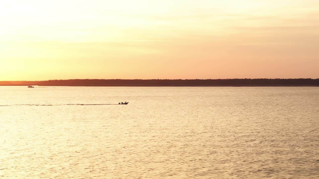 Golden light reflecting on quiet water near harbor pier with distant soft horizon edge