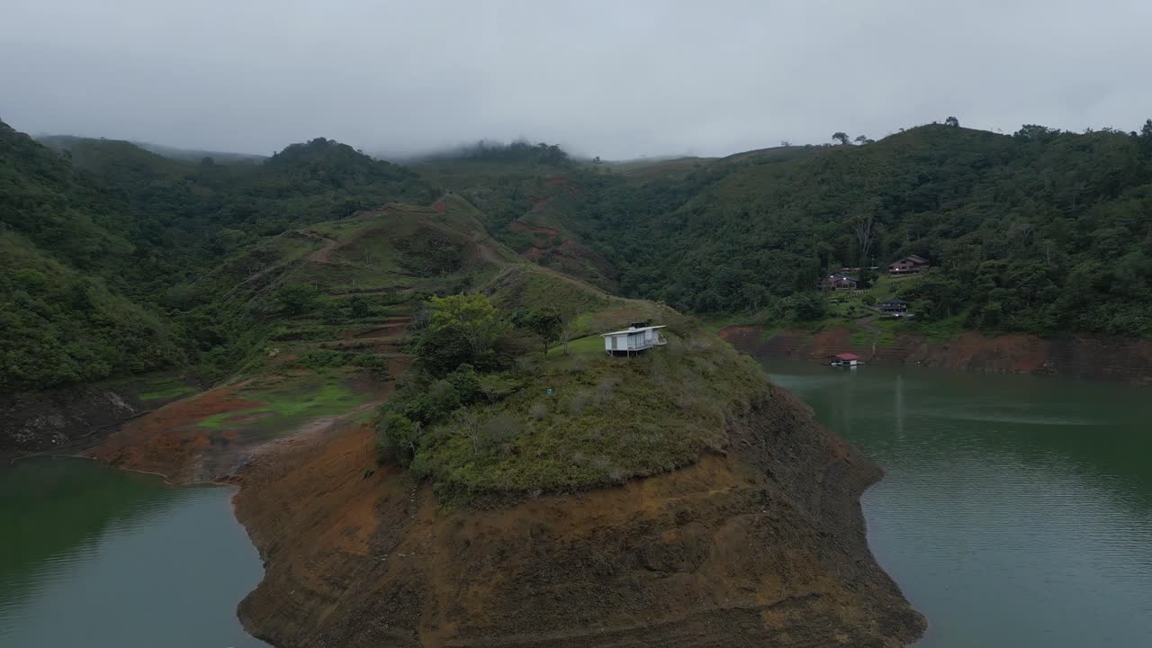 aéreo volando sobre la colina con una pequeña casa en la parte superior en el lago calima