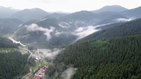 pan aérea lateral de nubes bajas suspendidas sobre un pequeño pueblo en las montañas