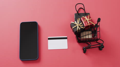 video de un teléfono inteligente con pantalla en blanco, tarjeta de crédito, carrito de compras sobre fondo rojo