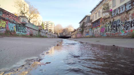 street art and colorful graffiti on a dry city canal wall on a sunny day, reflections in a water stream