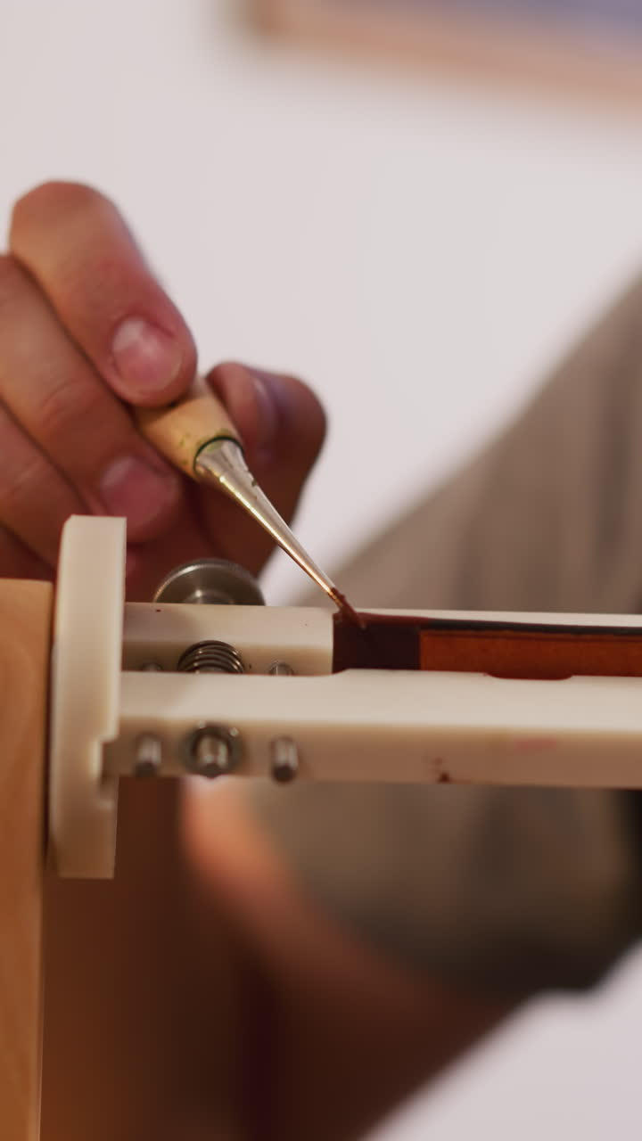 Master applies paint onto leather piece fixed by clamp in workshop closeup. Craftsman makes wristwatch belt slow motion. Handicraft tradition