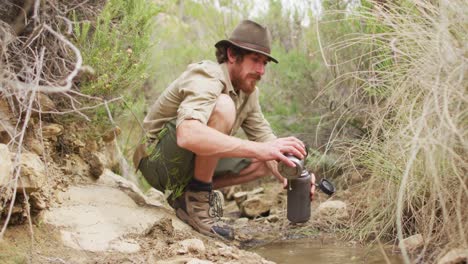 hombre caucásico de supervivencia vertiendo agua de arroyo en una botella de filtro para beber