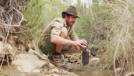 caucasian male survivalist pouring stream water into filter bottle for drinking