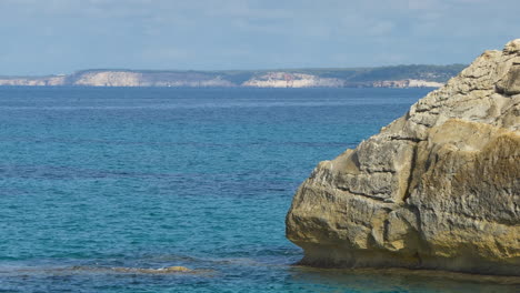 large chalk rock sinking into the transparent mediterranean sea on the southern coast of the minorcan island