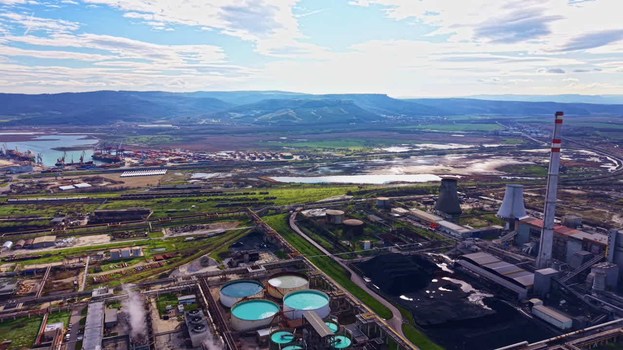 Vista de una zona industrial cerca de un río con tanques de almacenamiento y una fábrica bajo un cielo nublado en un paisaje rural