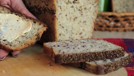 Close-up-shot-of-woman's-hands-spreading-butter-with-a-kitchen-knife-on-a-crispy-slice-of-homemade-bread