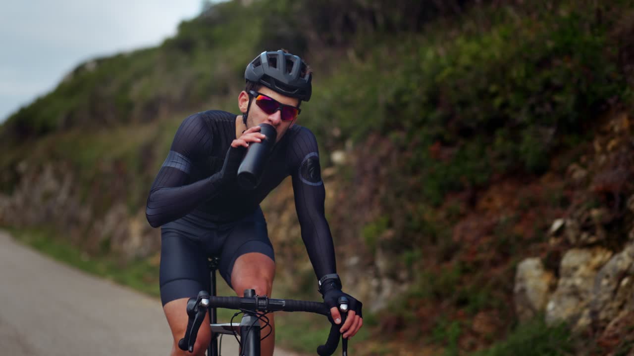 Ciclista professionista in bicicletta che beve acqua da una borraccia da viaggio.