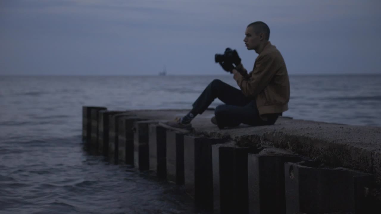 Man On A Concrete Pier Taking Pictures Of The Wavy Sea With His Camera - Medium Shot