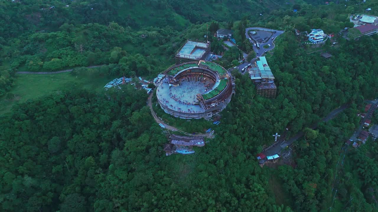 Wide aerial drone shot of Cebu’s Tops Lookout landmark surrounded by lush green mountains, roads, and nearby structures. Perfect for travel, tourism, and establishing scenes