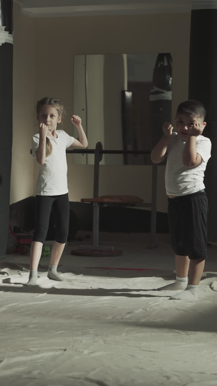 아이들은 무술 수업에서 전투자 위치에 서 있습니다. 작은 운동 선수 그룹은 체육관에서 느린 동작으로 전투 연습을 준비합니다.