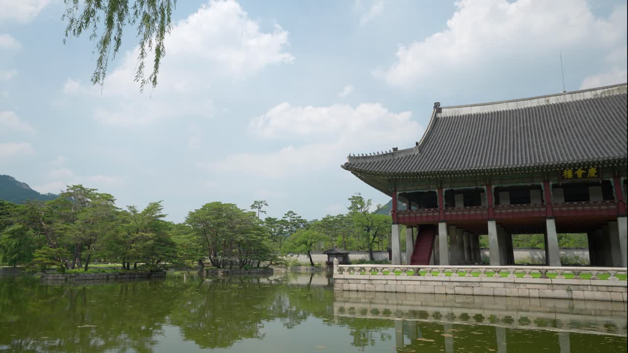 vista de primer plano del pabellón gyeonghoeru rodeado de estanque de agua verde y árboles verdes contra las nubes en el palacio gyeongbokgung, seúl, corea del sur
