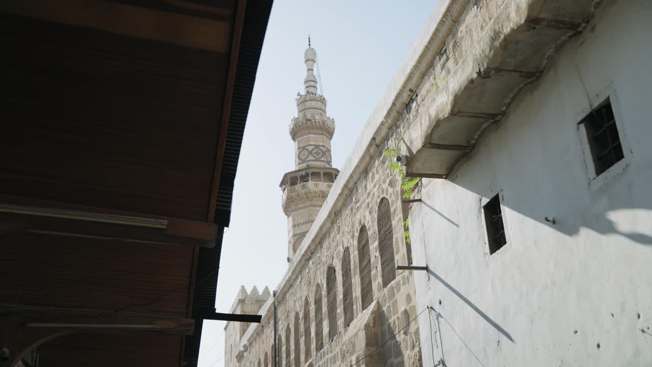 Wide cinematic shot of the Umayyad Mosque minaret and walls from a different angle in Damascus Old City, showcasing historic Islamic architecture and cultural heritage