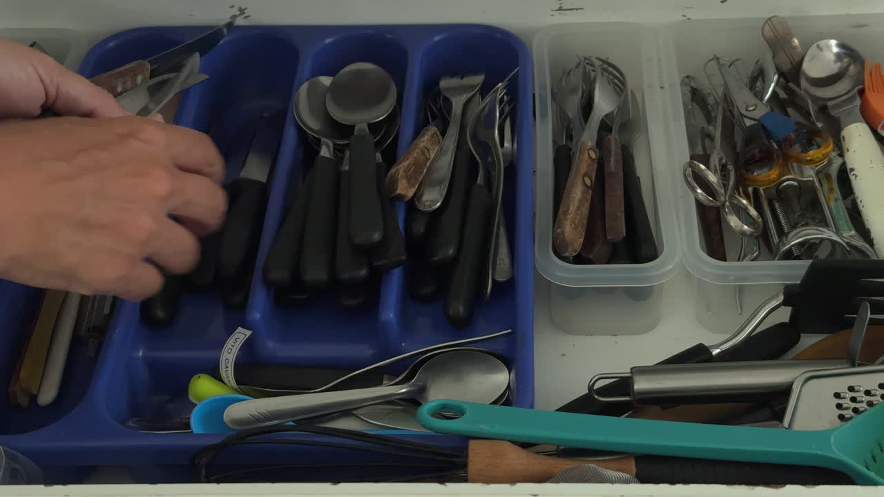 Hand Organizing Cutlery in a Kitchen Drawer