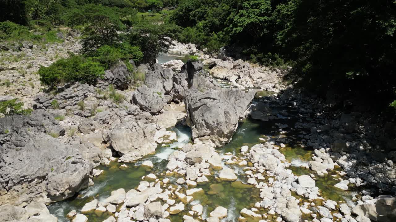 The shot pulls away, expanding the view to reveal many rocks around the river with strong flowing water at Tinipak River, Philippines