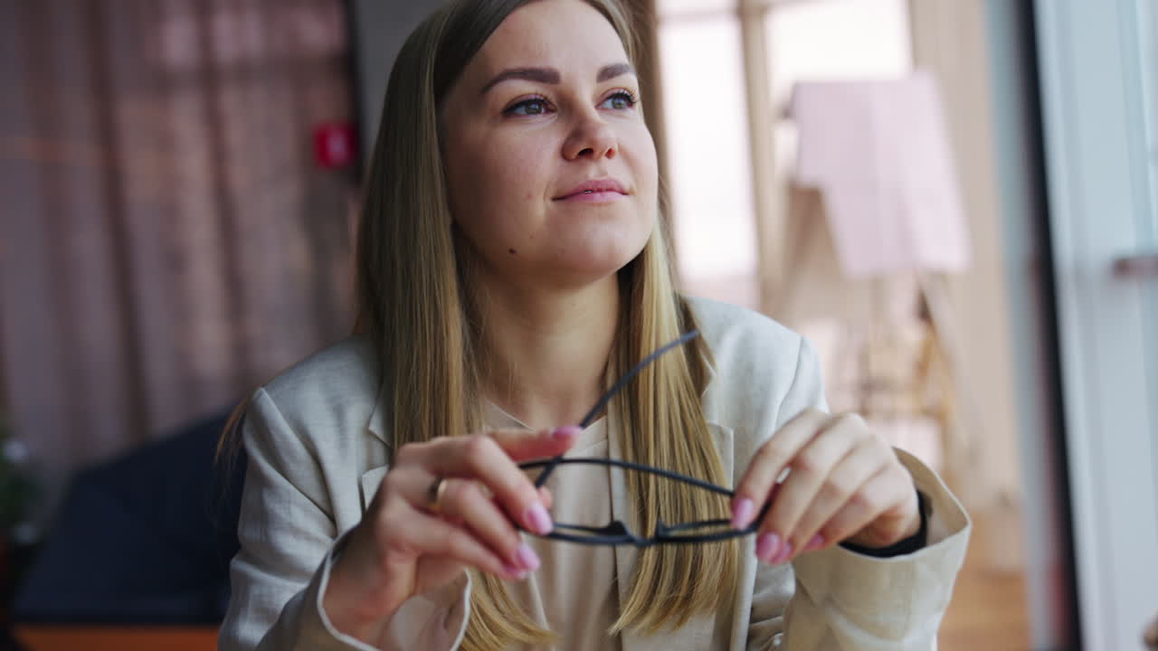 Blonde young woman takes off her glasses. Long-haired female feels tired and touches her forehead to relax. Close up.