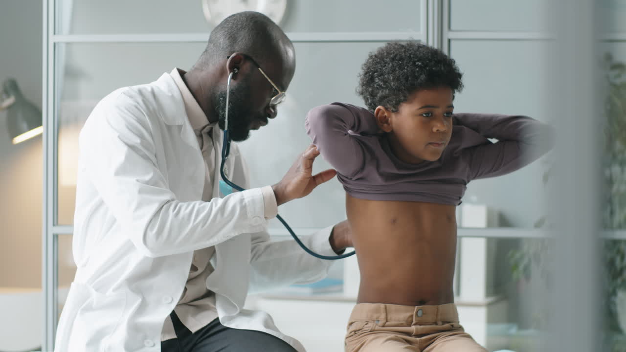 African American Pediatrician Checking Lungs of Little Boy with Stethoscope