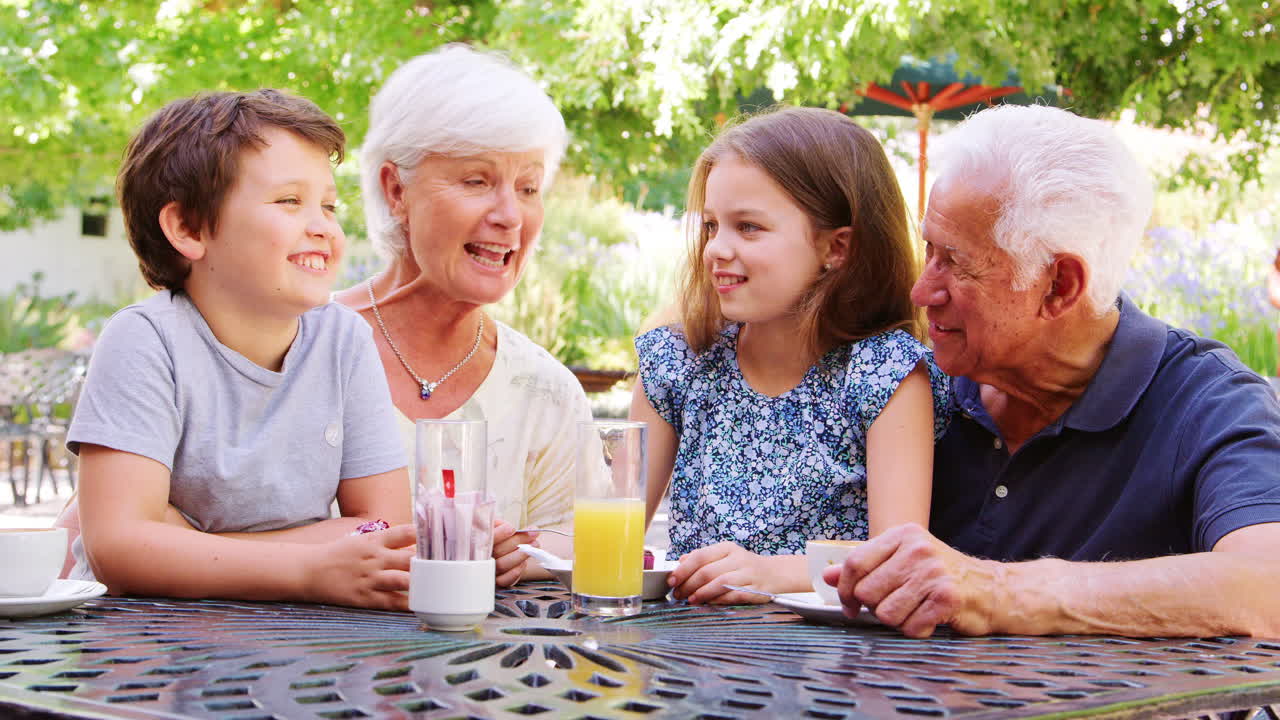 Kids sitting outdoors in a park cafe with their grandparents
