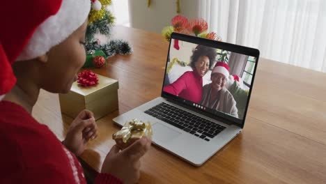 Mujer-Afroamericana-Con-Sombrero-De-Santa-Usando-Una-Computadora-Portátil-Para-Una-Videollamada-Navideña-Con-La-Familia-En-La-Pantalla