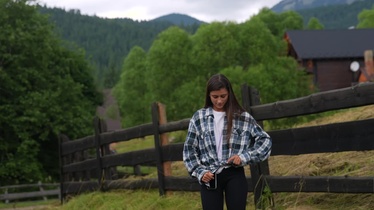 mujer en camisa a cuadros por una valla de madera en las montañas