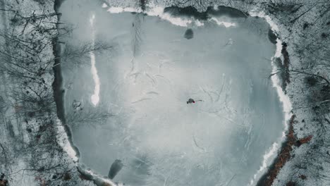 Drone-looking-down-towards-a-single-player-playing-ice-hockey-on-a-frozen-pond-or-lake-in-Canada