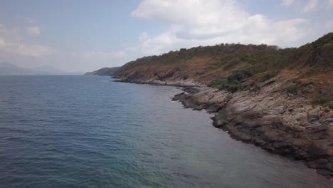 Aerial:-A-backward-high-altitude-flight-over-the-andaman-sea-the-a-rocky-shore-near-an-island-with-a-steep-slope-and-range-of-mountains,-Thailand