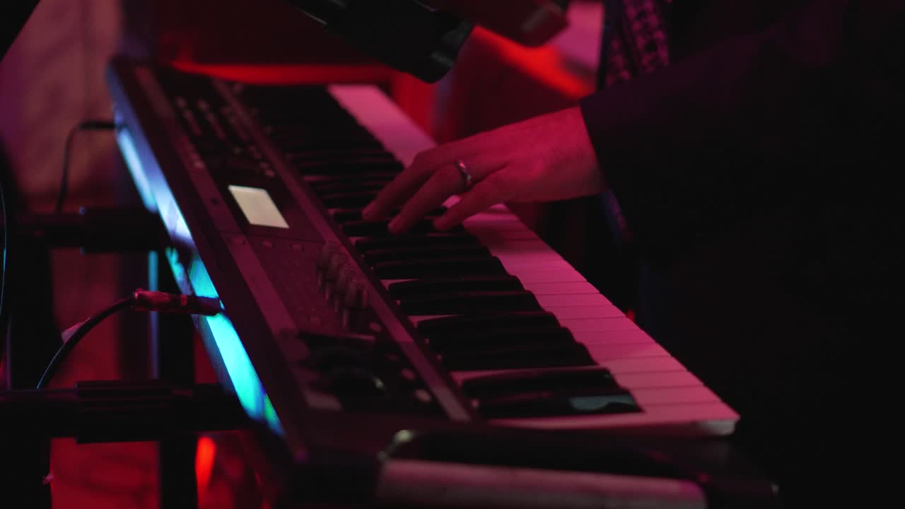 un hombre está tocando un teclado con las manos durante una fiesta en un club oscuro iluminado con luces de colores