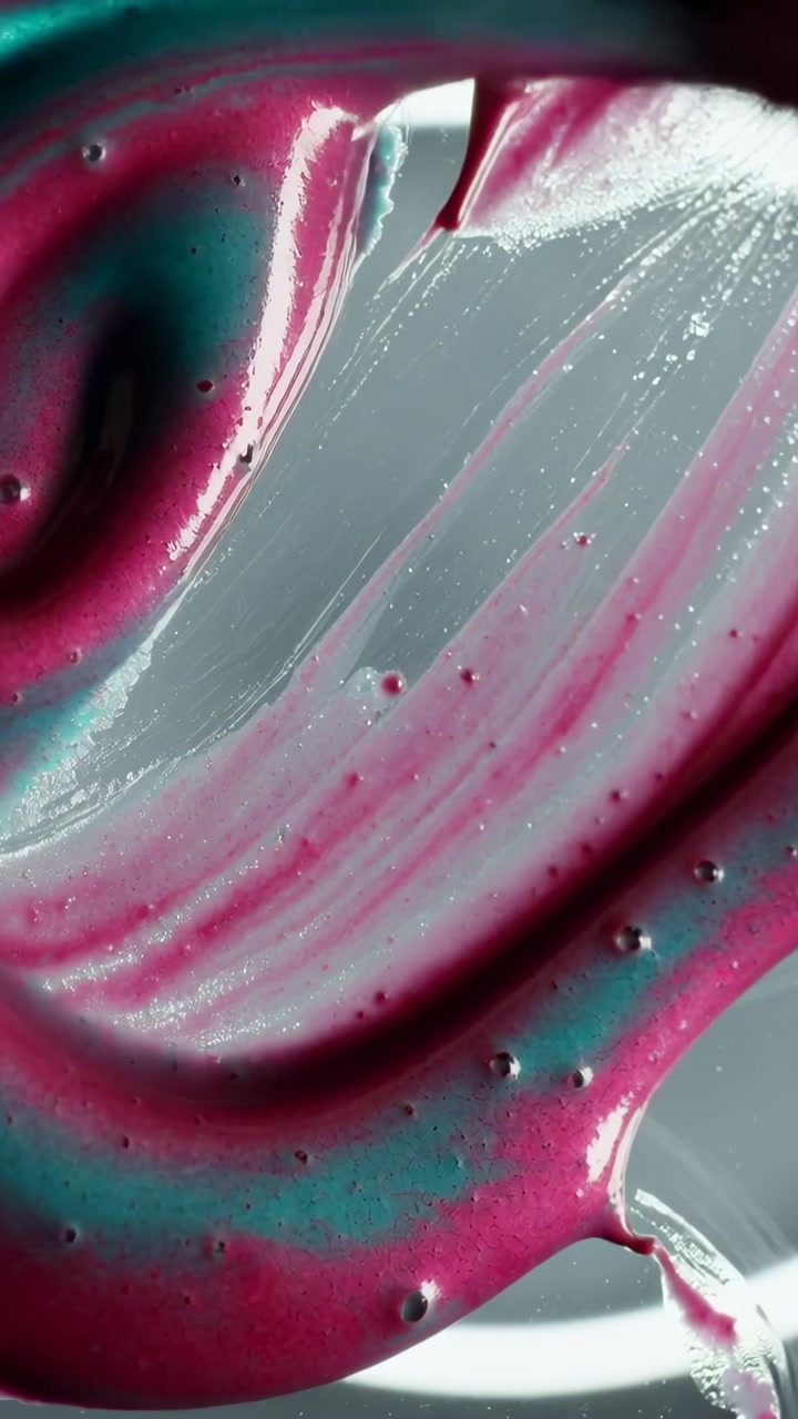 Vertical video: Dripping magenta teal ribbon, spatula pulling spiral on shiny plate, forming band