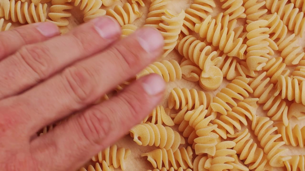 Hand Gently Moving Dry Fusilli Pasta on a Wooden Surface