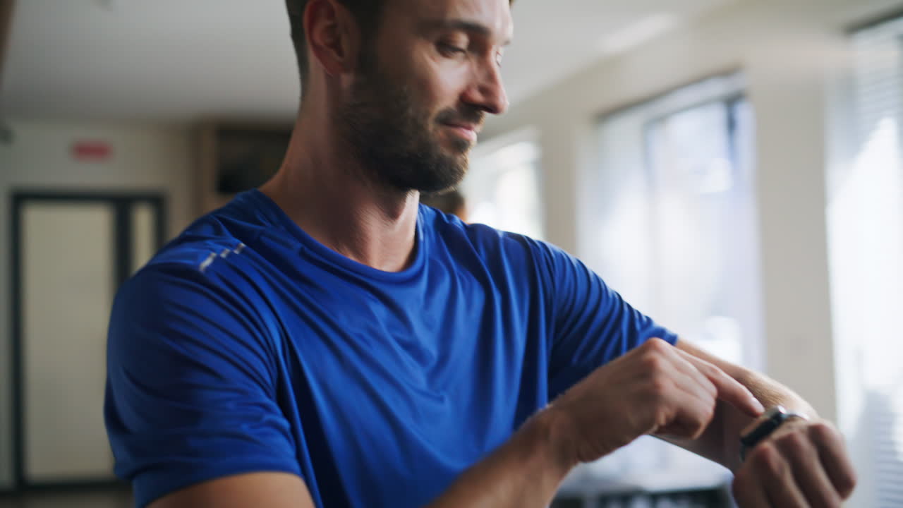 Primo piano di uno sportivo allegro che controlla lo smartwatch in un centro fitness. Uomo sorridente