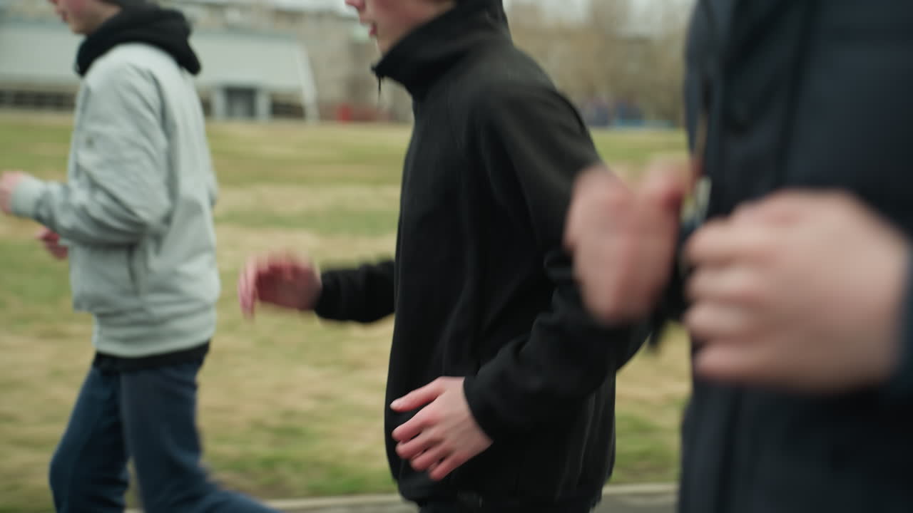 Close-up of three people jogging on a track near a grassy field, with a blurred background showing buildings and trees