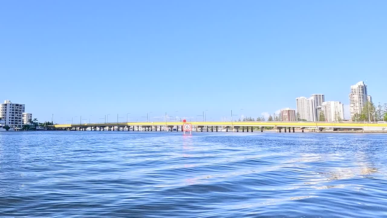 View of city skyline and speed limit sign along tranquil river waters under a clear blue sky.