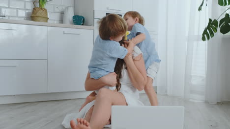 madre amorosa e hijos abrazados y divirtiéndose jugando sentados en el suelo. familia divertida y feliz. el juego después de ver la computadora portátil
