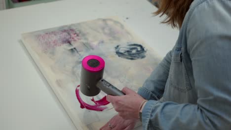 artista femenina secando y suavizando el activo de papel en el lienzo, en un estudio en casa