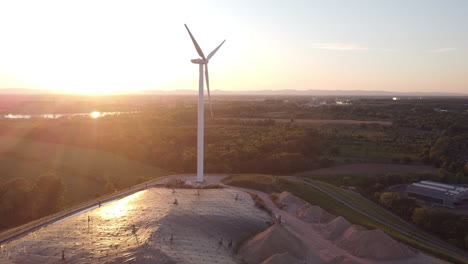 slow turning windmill power plant in europe with setting sun in the back while drone is flying up close