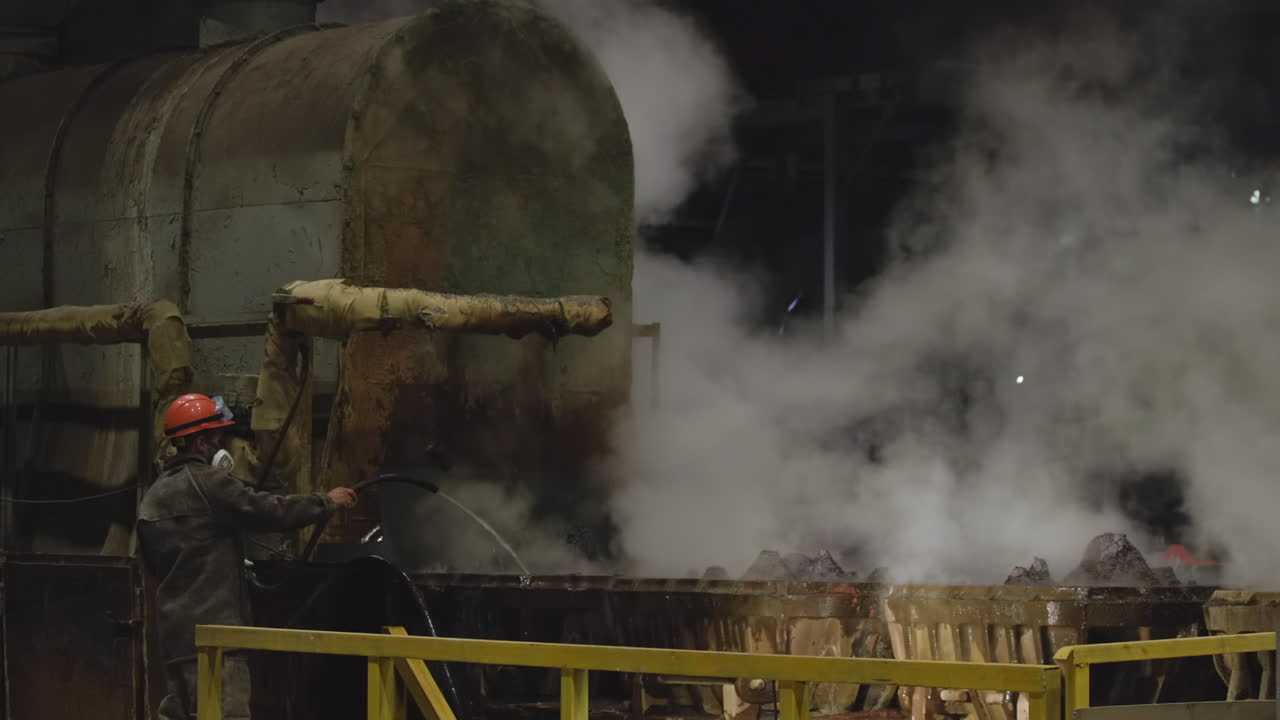 Operaio che raffredda metallo incandescente con acqua in una fabbrica industriale