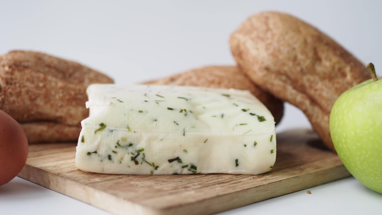 primer plano de un bloque de queso de hierbas con pan, manzana y huevo en una tabla de madera