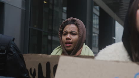 young american female activist holding a cardboard placard during a climate change protest surrounded by others activists