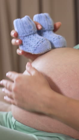 big belly of a pregnant woman. future mother holding little knitted socks on her stomach. close-up. side view. vertical video