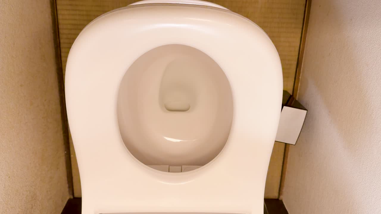 Top view of a white ceramic toilet seat automatically closing in a bright restroom