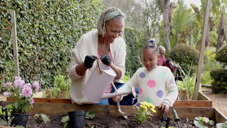 Feliz-Abuela-Y-Nieta-Afroamericana-Regando-Flores-En-El-Jardín,-Cámara-Lenta