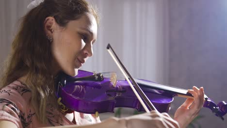 una joven violinista tocando el violín en casa, en primer plano.