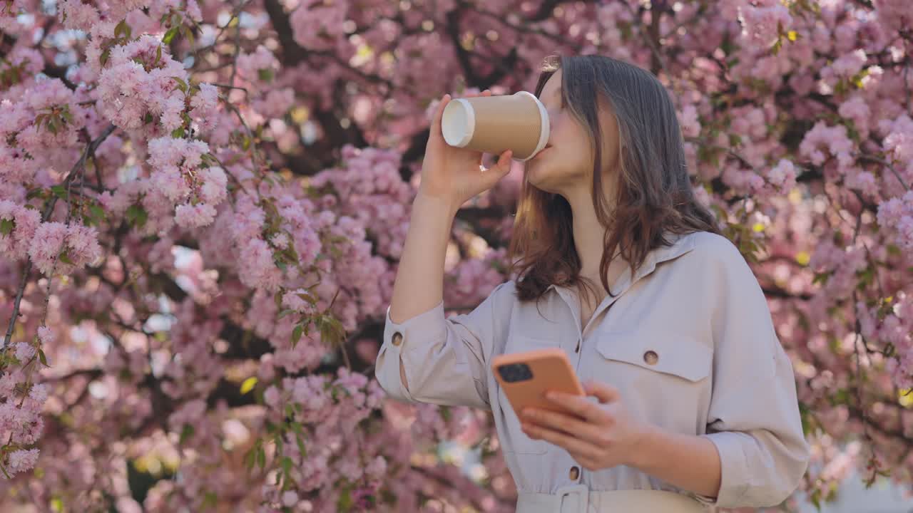 Woman enjoying coffee and phone under cherry blossom trees
